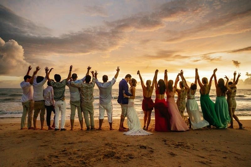 Wedding party raising their arms on a beach at sunset