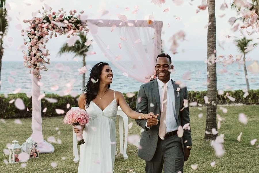 Newlyweds walking beneath a flower-covered ceremony arch