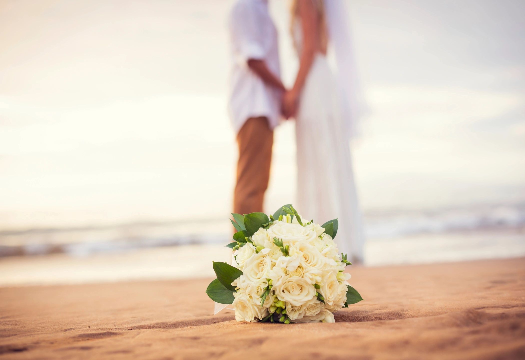 Bridal bouquet beside a wedding dress on the beach