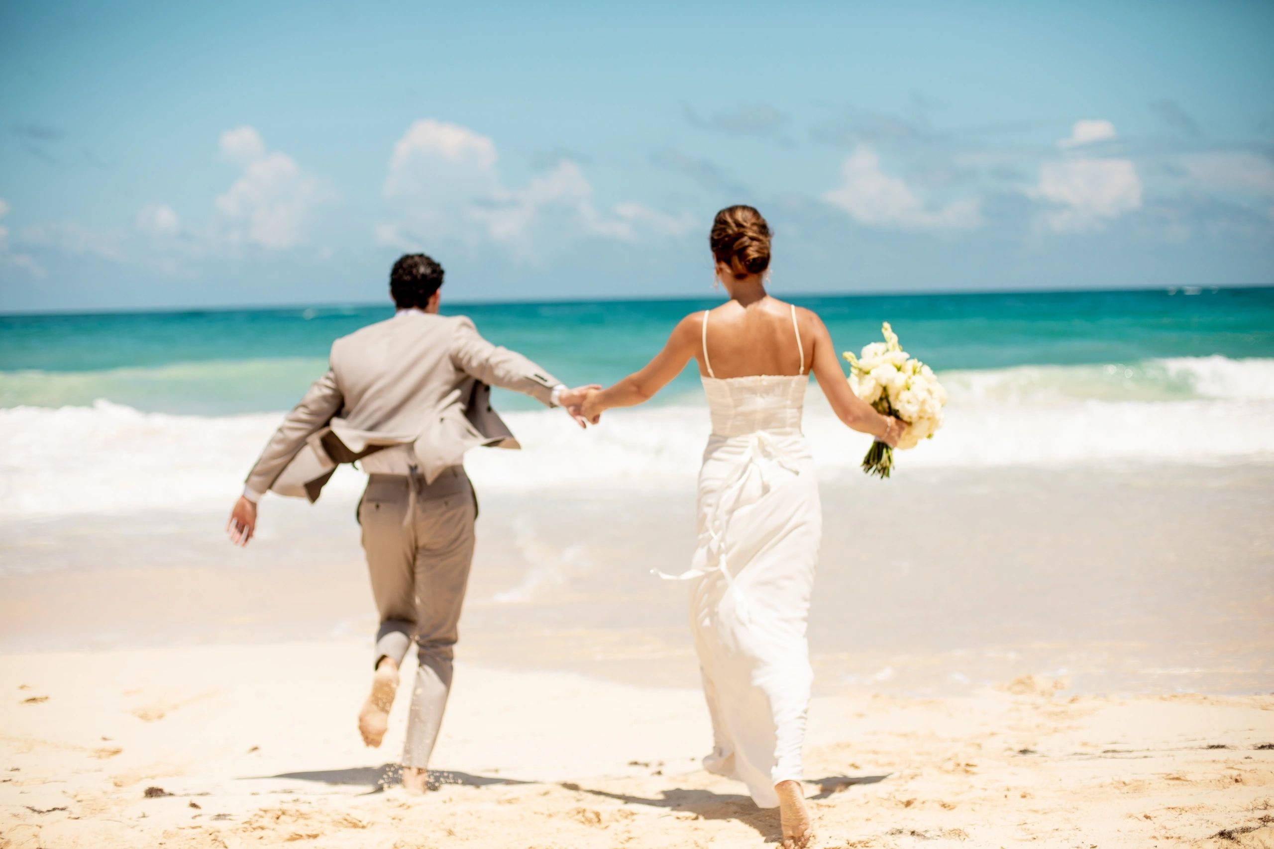 Newlyweds holding hands as they walk along a beach