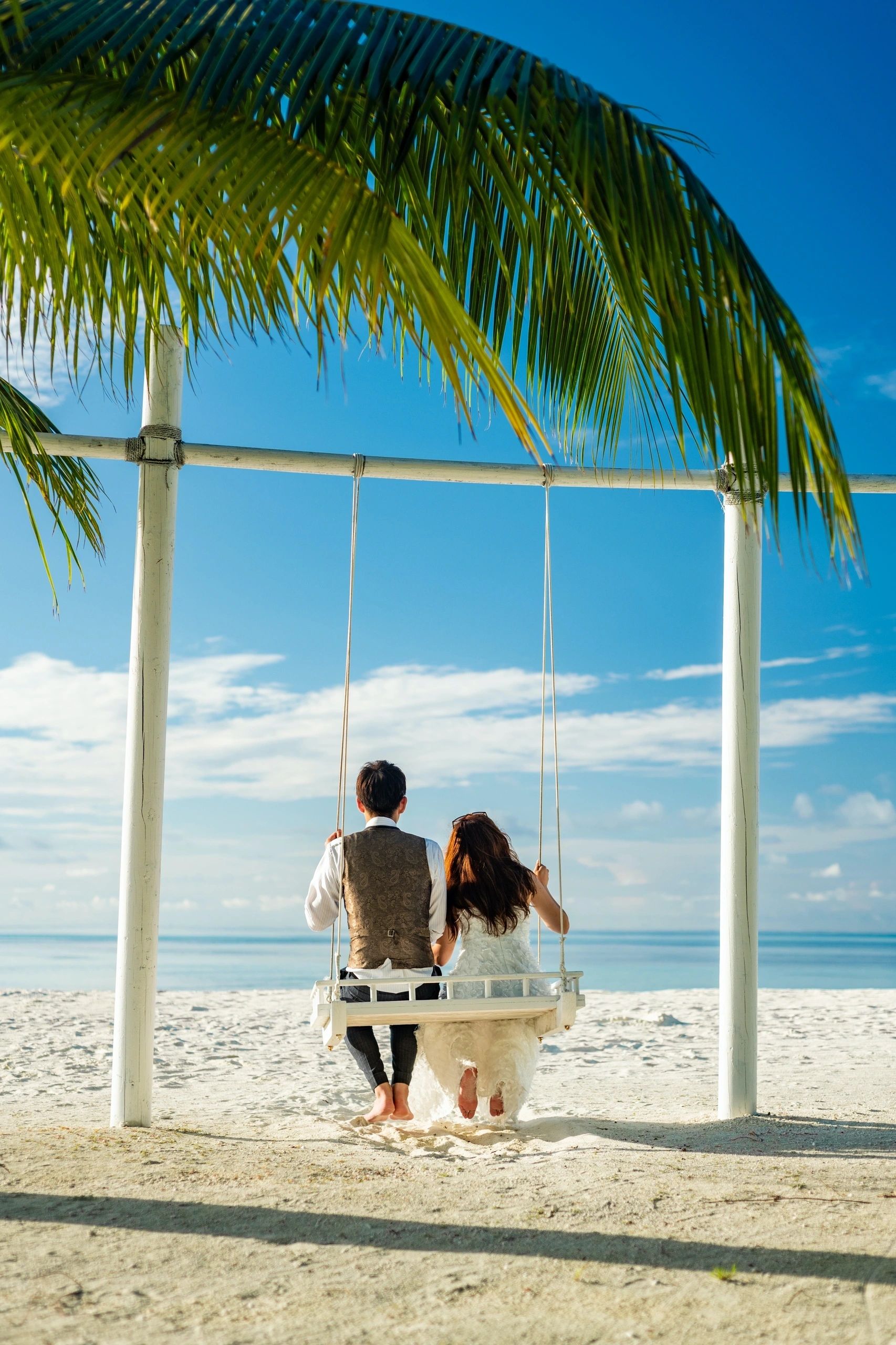Couple on a beach swing beneath a palm tree