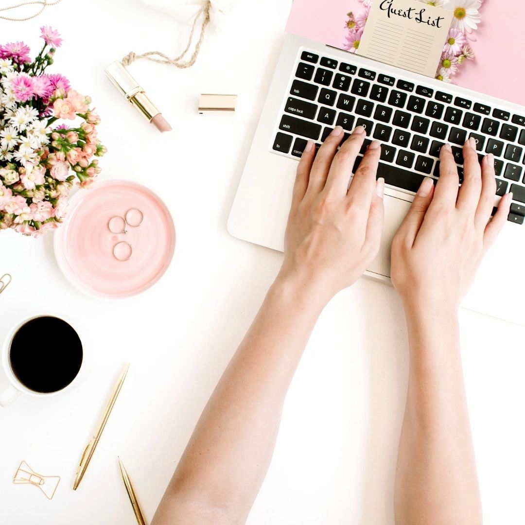 Hands typing on a laptop beside flowers