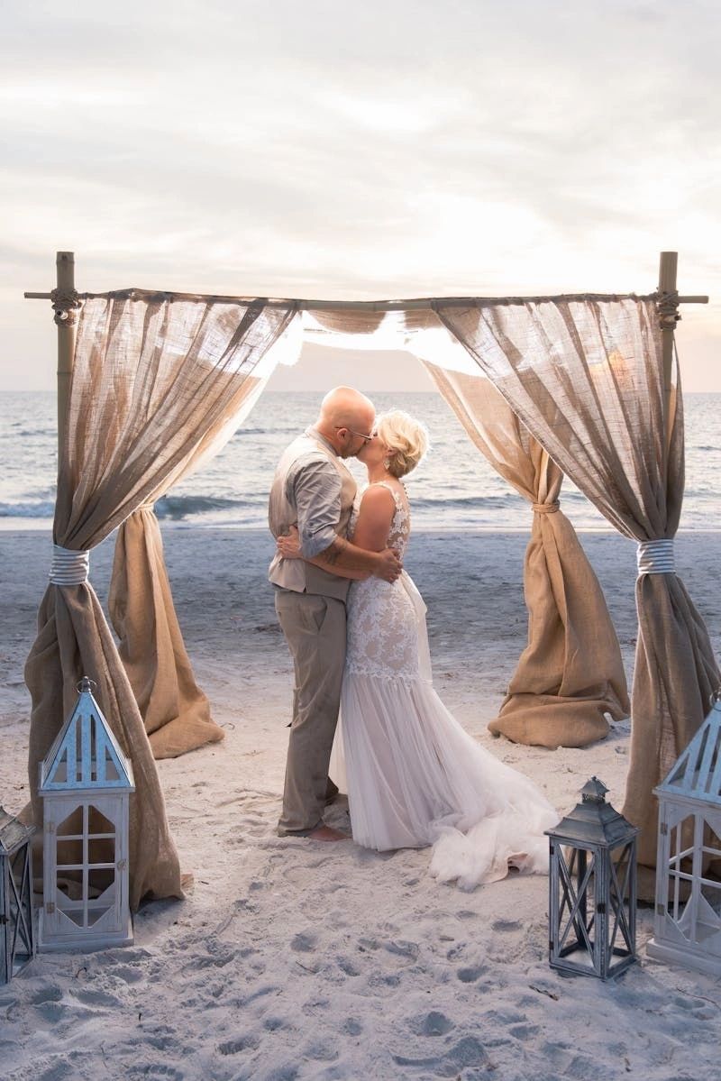 Newlyweds beneath a draped beach wedding arch