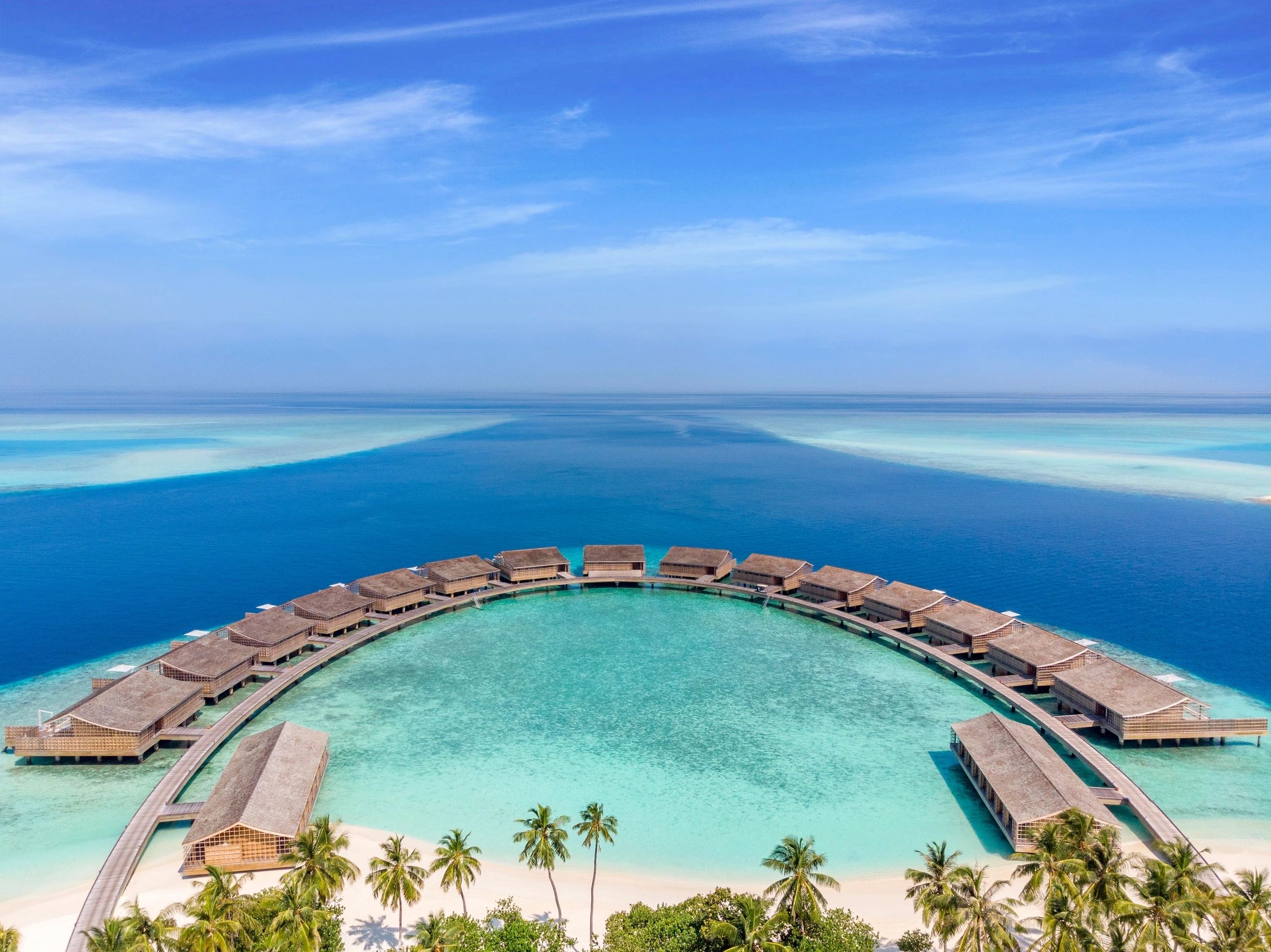 Overwater villas arranged around a turquoise island lagoon
