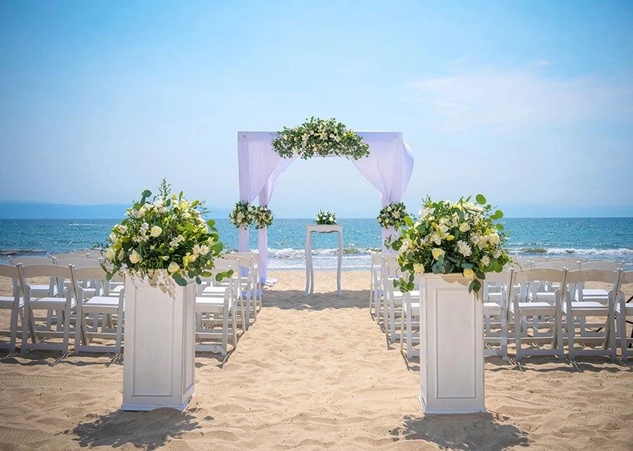 White ceremony arch and floral arrangements on a sandy beach