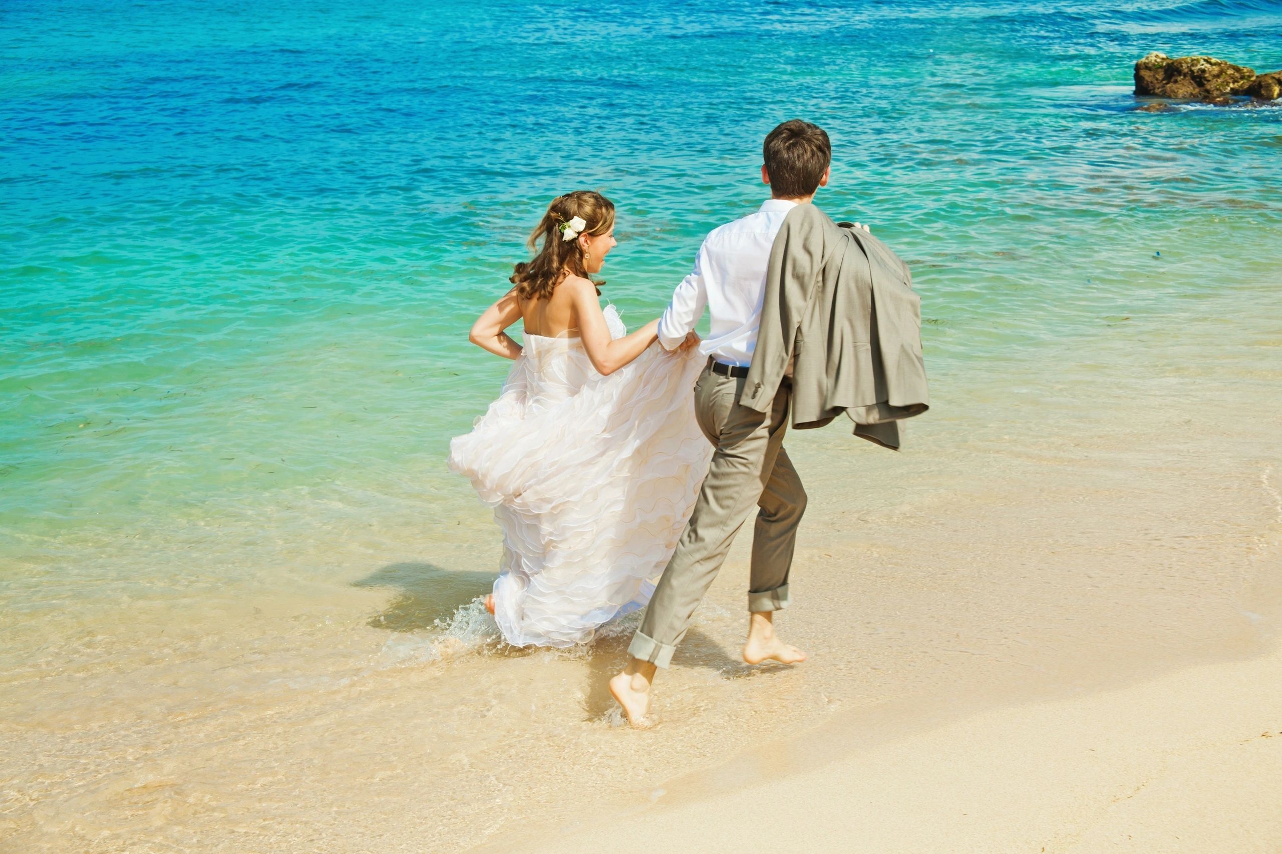 Newlyweds walking beside clear turquoise water