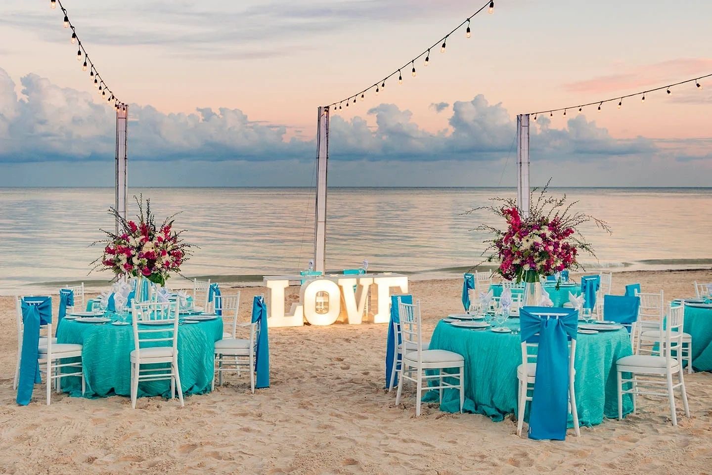 Beach reception table with turquoise chairs and a LOVE sign
