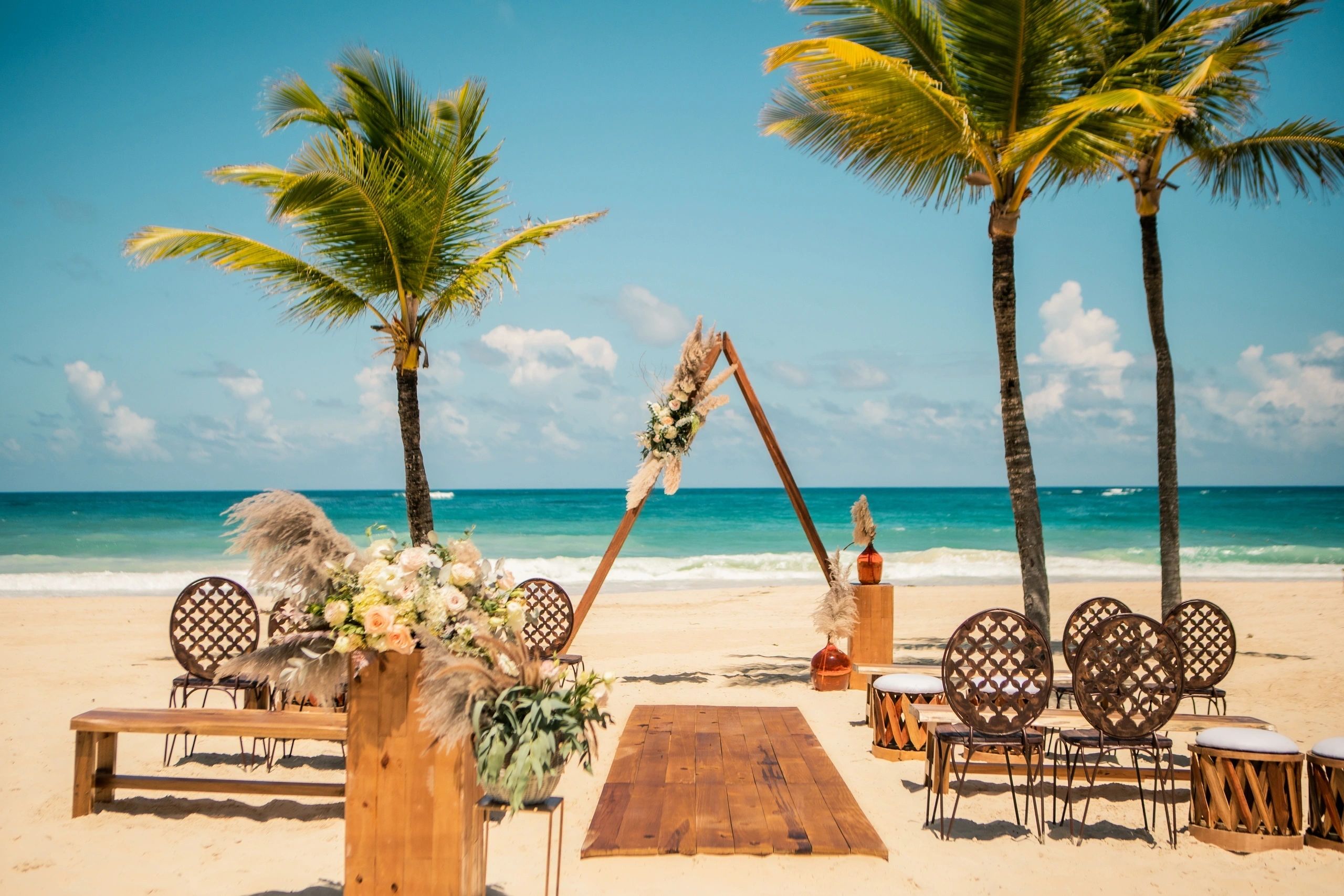Boho beach ceremony with palm trees and woven chairs